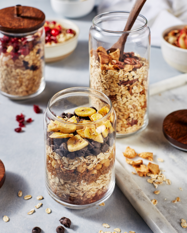 Des bocaux de flocons d'avoine faits maison avec des couches de sucre brun, d'avoine, de pépites de chocolat et de fruits.