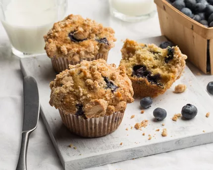 Trois muffins aux bleuets servis avec du lait et un panier de bleuets