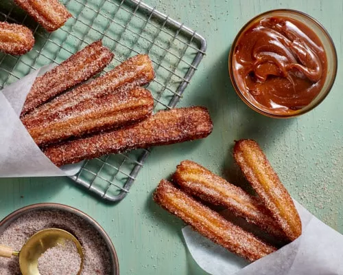 Churros avec du sucre à la cannelle sur une grille de refroidissement avec une trempette de dulce de leche.