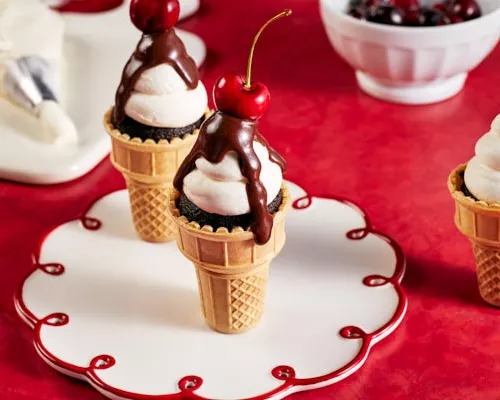 Cupcakes au chocolat dans des cornets à glace classiques, décorés de glaçage, de ganache au chocolat et garnis d'une cerise, ser