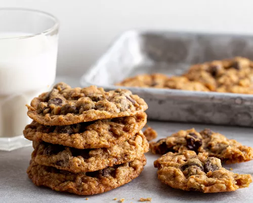 Une pile de biscuits aux flocons d'avoine et aux pépites de chocolat avec un verre de lait et un plateau de service en métal.