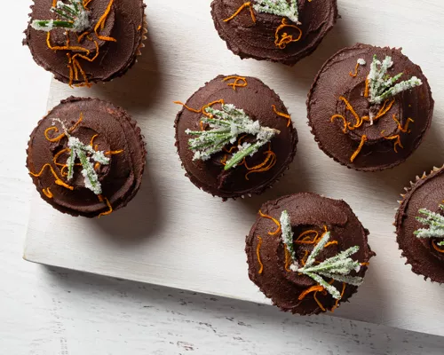 Rangées de cupcakes garnis de glaçage à la ganache, zeste d’orange et romarin givré