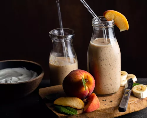 Deux bouteilles d’une portion de smoothie banane, pêche et Earl Grey avec pailles en verre, une planche à découper et des fruits