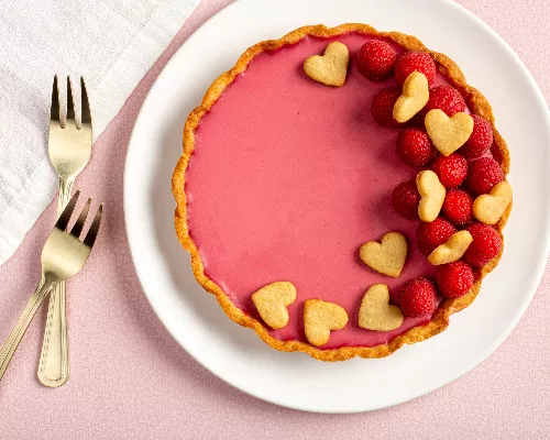 Tarte panna cotta framboises et eau de rose décorée de framboises et de biscuits en forme de cœur