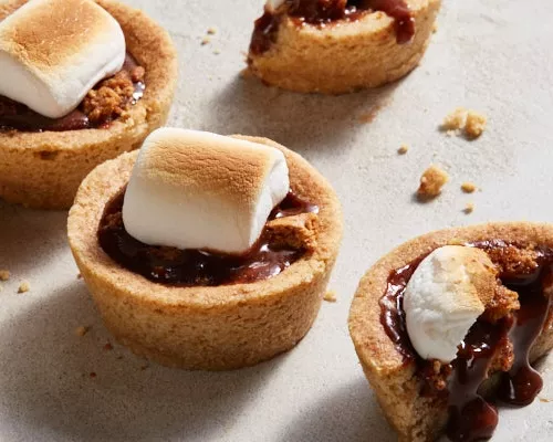 Quatre coupes de biscuits s'mores avec des guimauves grillées, une coupe en deux et une coulée de chocolat