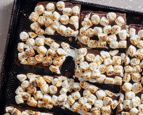Barres de s'mores dans un plateau de service noir et or, avec des guimauves grillés partiellement fondus et étirés.