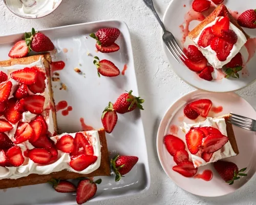 Un gâteau en plaque fraise-yuzu sur un plateau blanc servi avec des fraises avec deux tranches sur des assiettes.