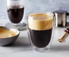Un verre de café vietnamien à la mousse d'œuf avec un bol de mousse d'œuf, un verre de café et un équipement pour faire du café.