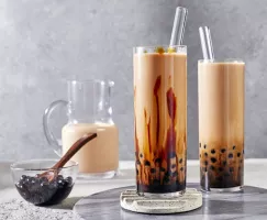 Deux verres de thé au lait boba hojicha présentés avec un pichet de thé et un bol de perles de tapioca.