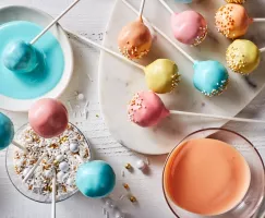 Des cake pops aux couleurs pastel avec des éclats de verre sur un plateau, certains dans un verre d'éclats de verre et un autre 