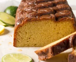 Un gâteau quatre-quarts tranché à une extrémité, disposé sur une assiette décorée de tranches de citron et de lime