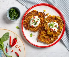 Croquettes de maïs et chili sucré sur assiette rouge et blanche avec crème sûre et herbes