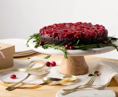 Gâteau au chocolat renversé aux canneberges présenté sur une assiette sur pied décorée de romarin et de canneberges