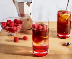 Deux verres d'espresso tonique glacé à la framboise sur une table en bois, accompagnés d'un bol de framboises et d'une machine à