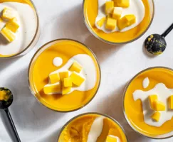 Cinq bols de verre de pouding à la mangue garni de mangue et de lait évaporé, et deux cuillères noires