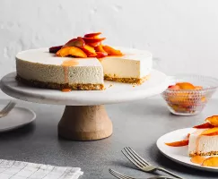 Gâteau au fromage à la vanille sans cuisson avec pêches macérées sur une assiette à gâteau, et un morceau de gâteau dans une ass
