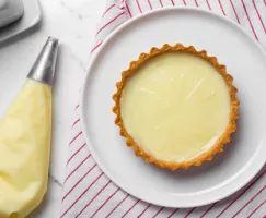 Une poche à douille à côté d'une croûte à tarte garnie de crème