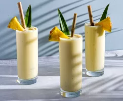 Trois verres de pina colada garnis de bâtonnets et de feuilles d’ananas avec des pailles en bambou