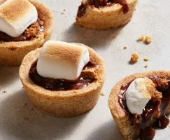 Quatre coupes de biscuits s'mores avec des guimauves grillées, une coupe en deux et une coulée de chocolat