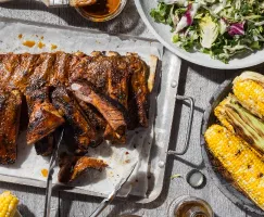 Une assiette de côtes levées nappées de sauce barbecue à la moutarde accompagnées de salade et d’épis de maïs cuits au barbecue.