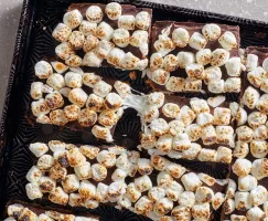 Barres de s'mores dans un plateau de service noir et or, avec des guimauves grillés partiellement fondus et étirés.