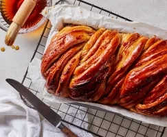 Babka aux pommes épicées dans un plat à four sur une grille de refroidissement avec un bol de sirop de miel et de cassonade.
