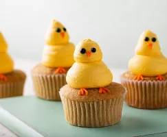 Cupcakes avec poussins jaunes faits de glaçages sur une planche verte en bois
