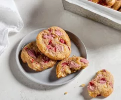 Trois cookies aux fraises et au chocolat rubis sur une assiette, dont un cassé en deux.