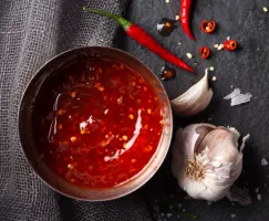 Sauce chili douce dans un bol en métal avec des piments chilis entiers, des piments émincés et une gousse d’ail