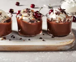 Deux puddings au chocolat végétaliens garnis de crème fouettée, de flocons de noix de coco, de flocons de cacao et de cerises.